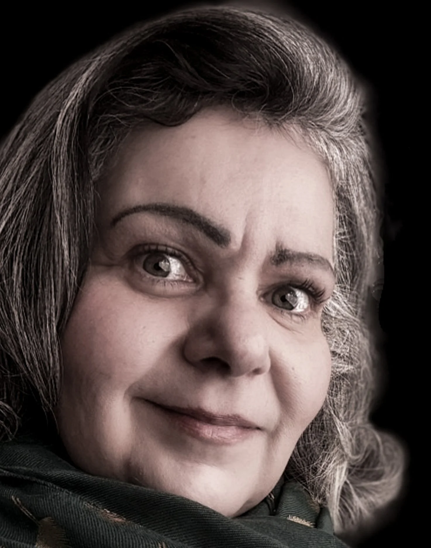Une femme avec des cheveux gris et bouclés, souriant légèrement, portant une veste noire, contre un fond sombre.