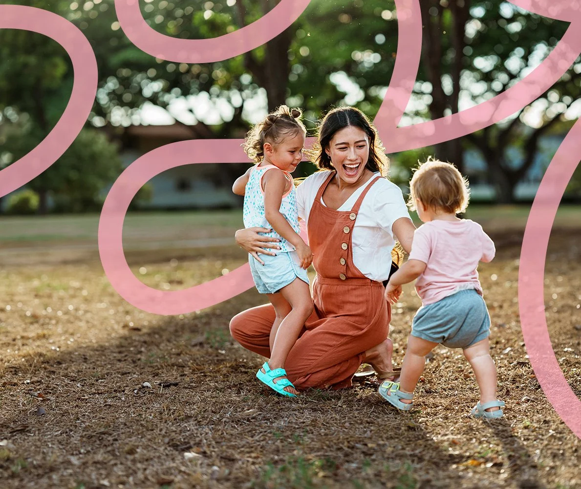 Smiling mother outdoors playing with her young children, representing family support and perinatal therapy