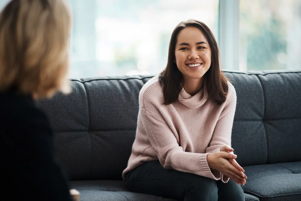 Smiling woman sitting comfortably on a couch during an online telehealth psychology session