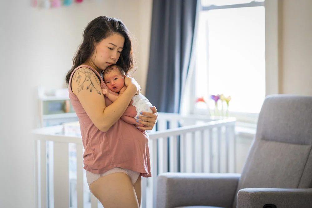 Mother standing near a crib holding her newborn baby, representing postpartum therapy for women across cultures, ethniicities, faiths, ways of thinking and feeling