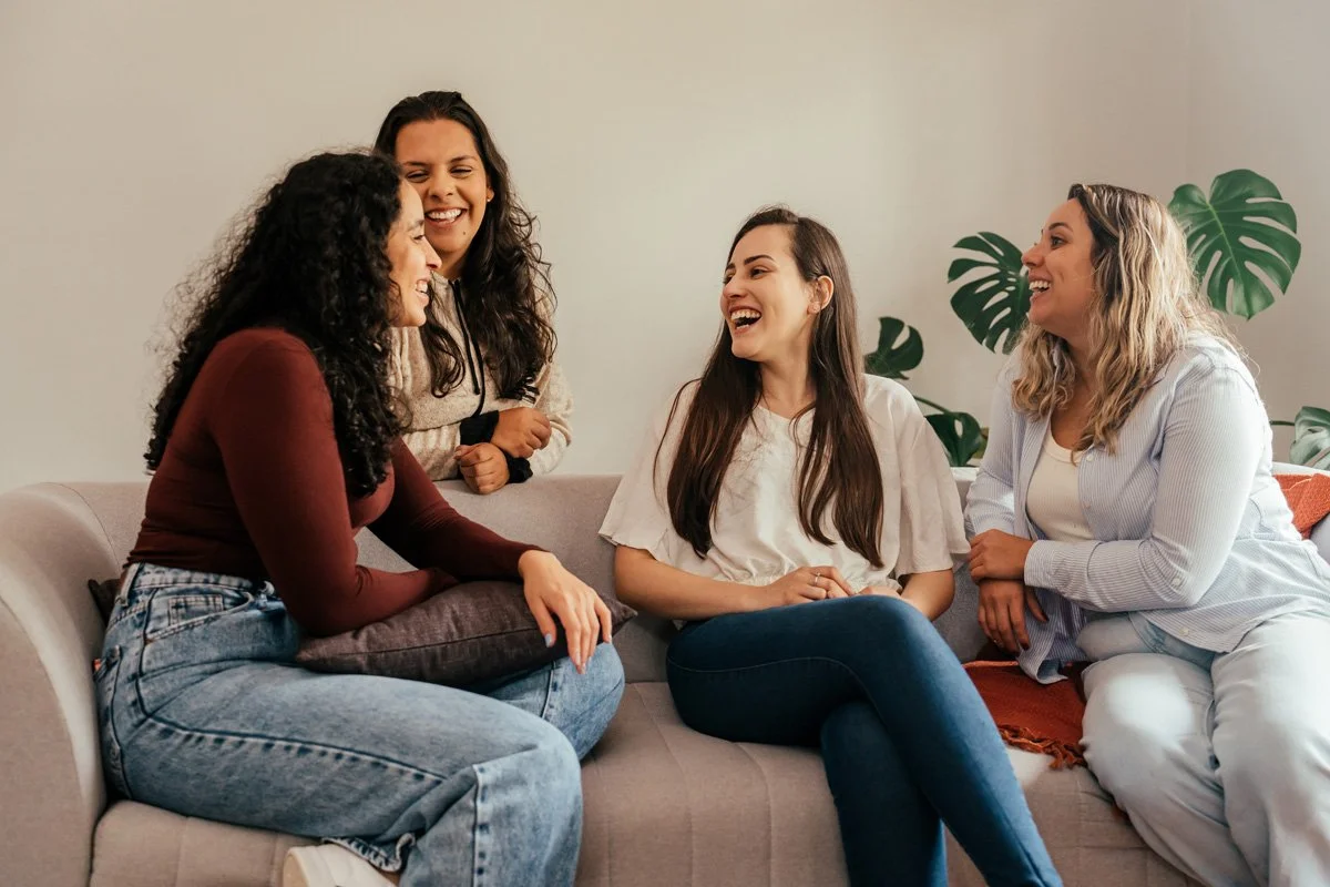 A group of diverse women sharing a warm, supportive conversation in a bright living room