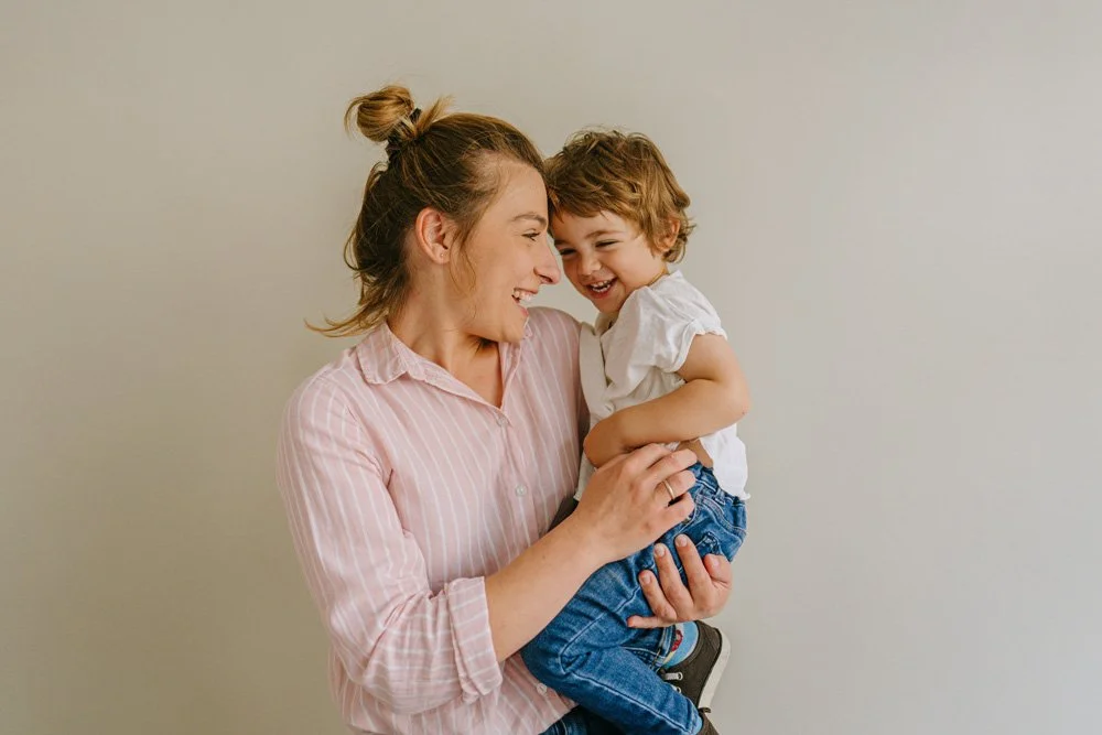 Smiling mother holding her laughing toddler in her arms, illustrating early motherhood support and family well-being