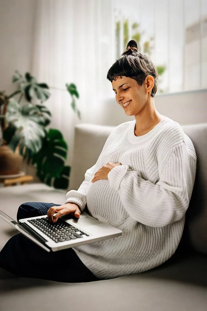 Pregnant woman sitting comfortably on a sofa using a laptop for an online telehealth psychology appointment