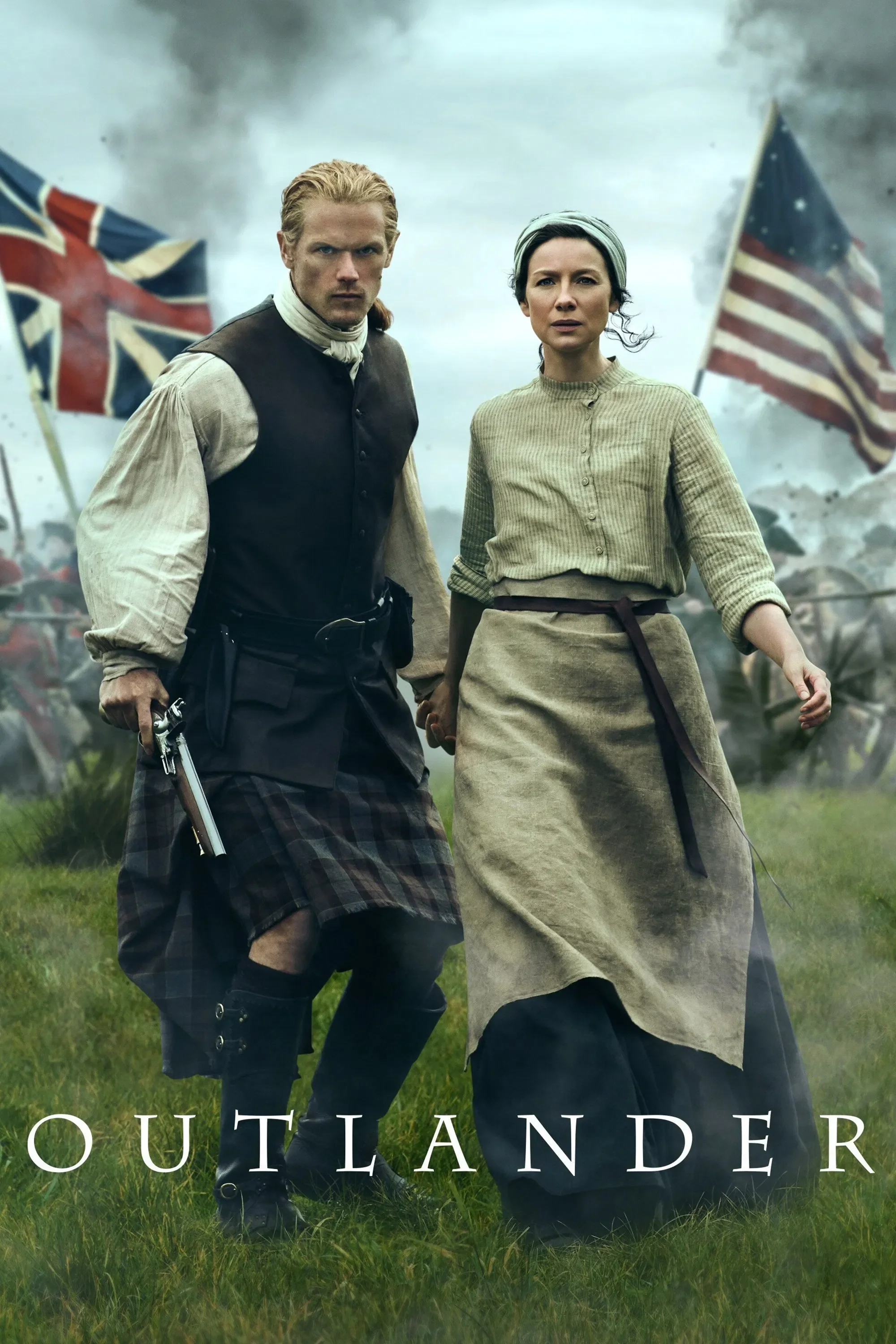 A man and woman dressed in historical clothing stand in a field during a battle scene, with American flags and smoke in the background, from the show Outlander.