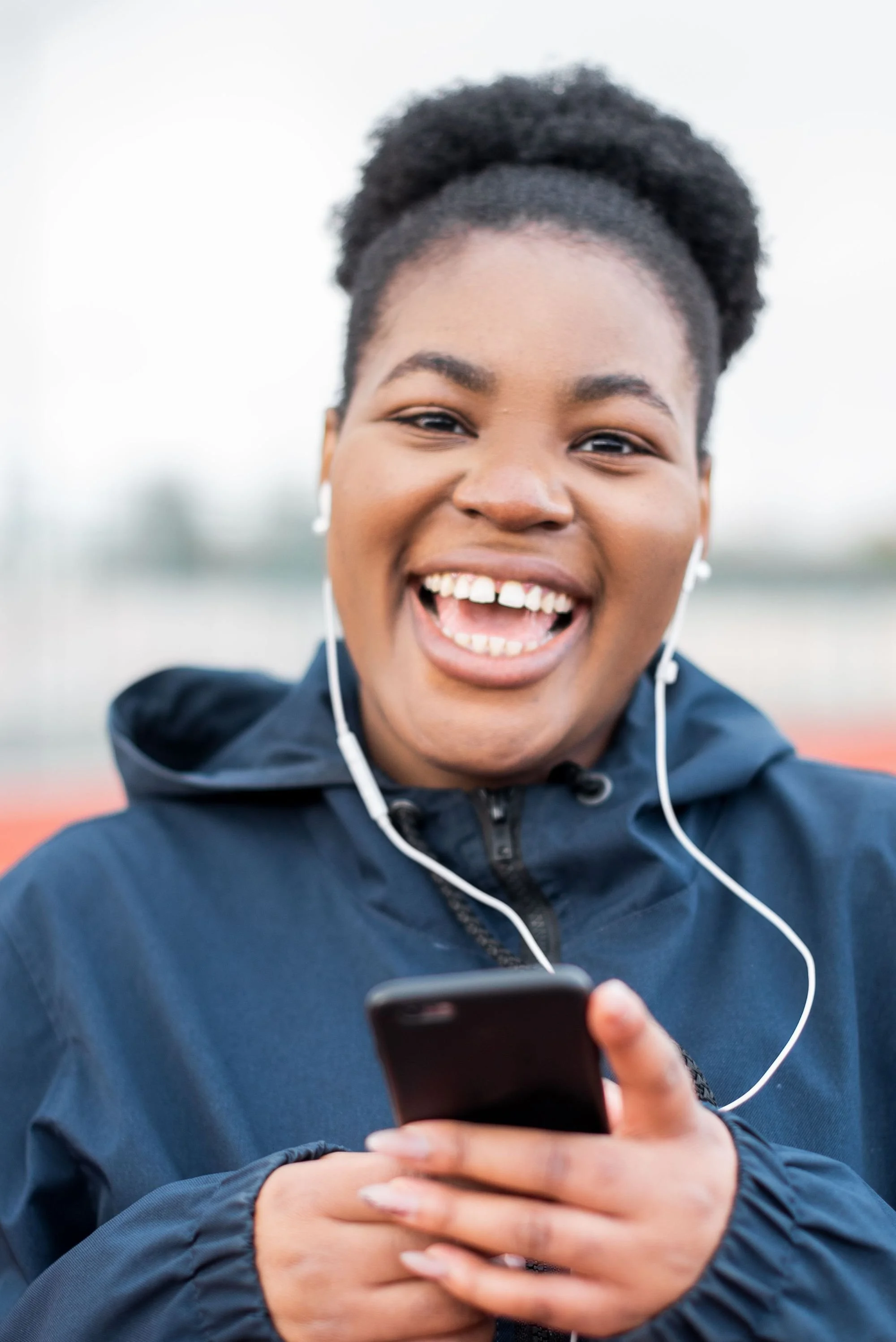 A young woman smiling and viewing the online women leaders community on her phone.