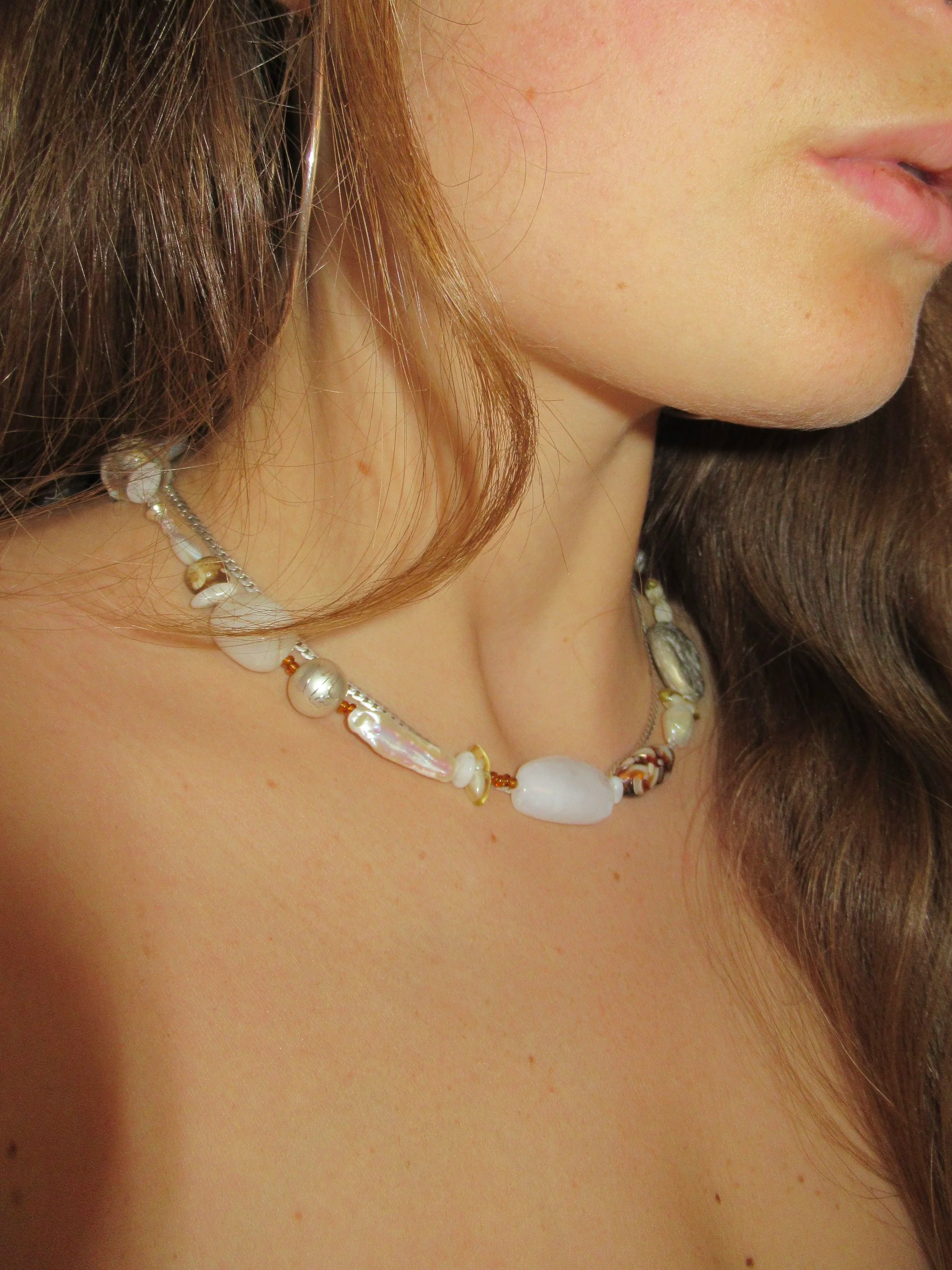 Close-up of a woman's face showing her lips, nose, and part of her chin, with long brown hair and a pearl and shell necklace.