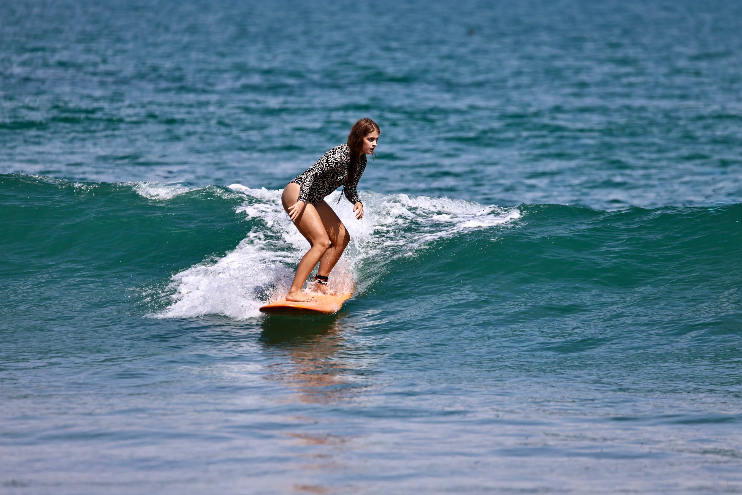 A woman surfing on a small wave in the ocean, wearing a black and white patterned wetsuit.