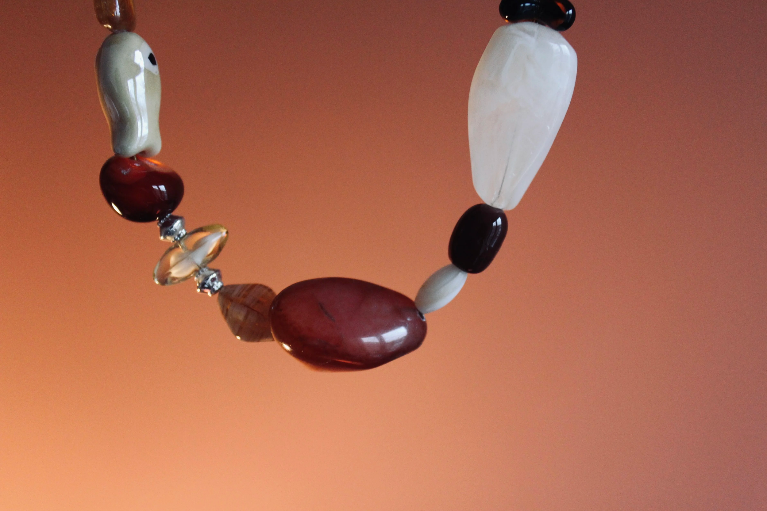 Close-up of a beaded necklace with various colored stones against a gradient orange background.
