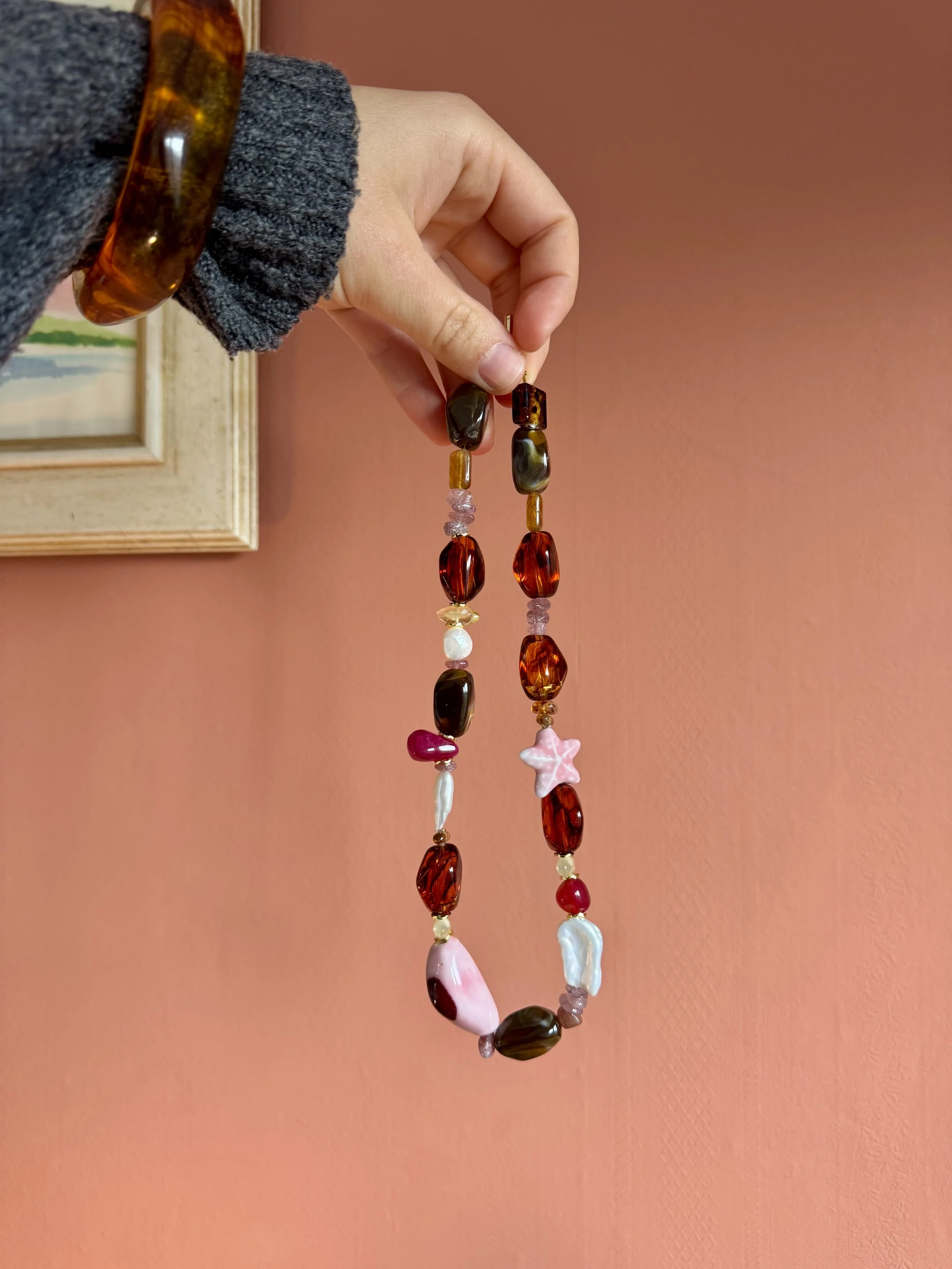 Colored glass bead necklace hanging against a pink wall.