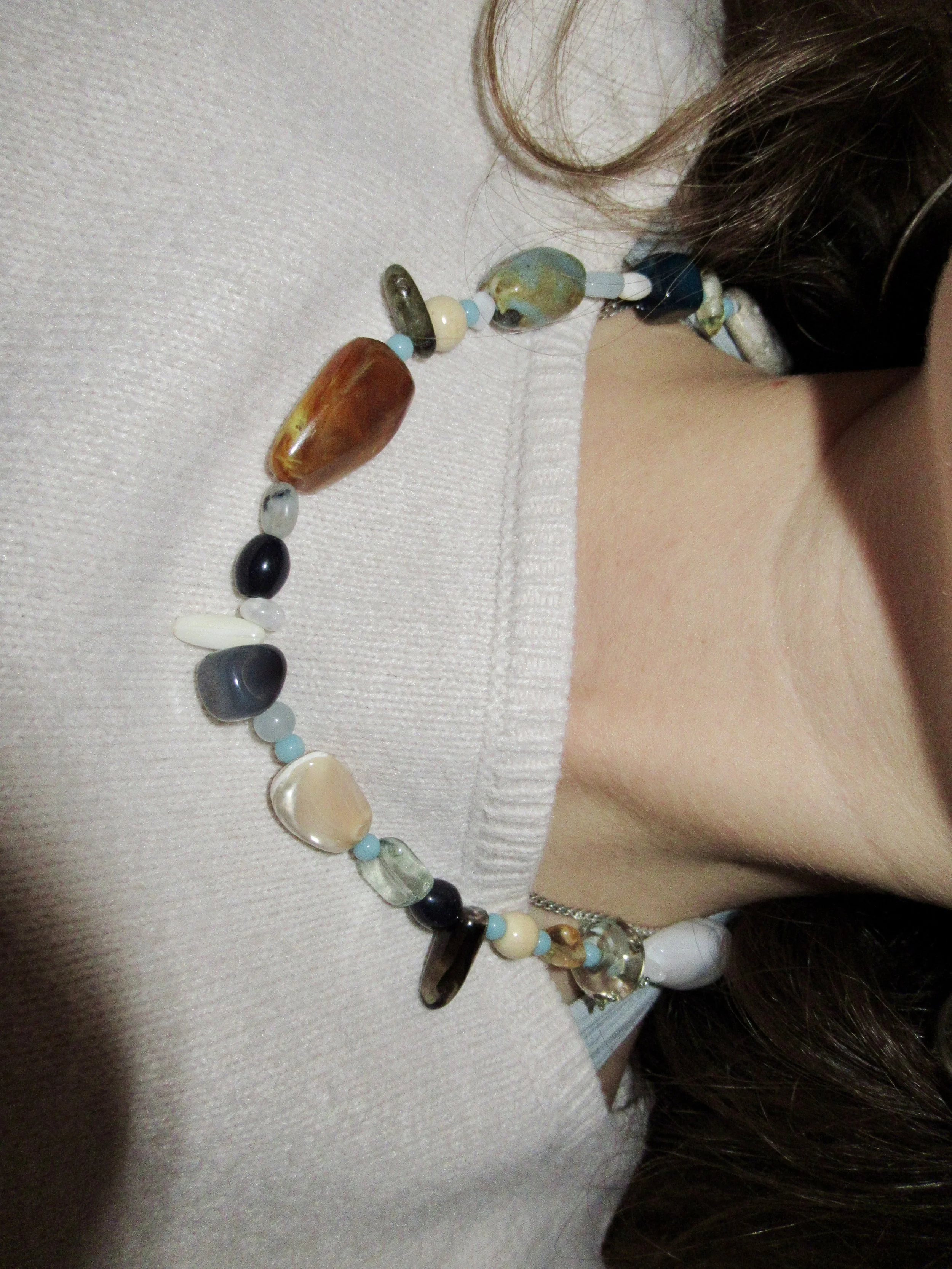 Close-up of a person's neck and shoulder area wearing a beaded necklace with various colorful beads, and part of their brown hair visible.