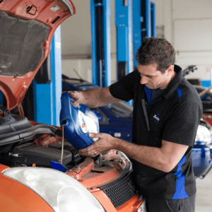 A mechanic inspecting and filling windshield washer fluid in a vehicle's engine compartment.