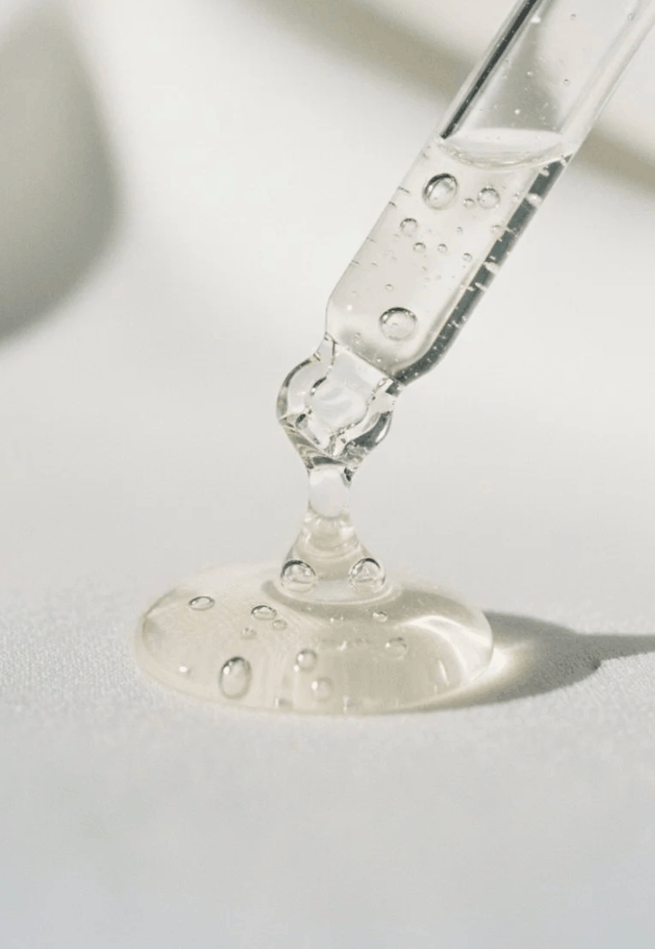 A glass dropper dispensing clear liquid onto a white surface.