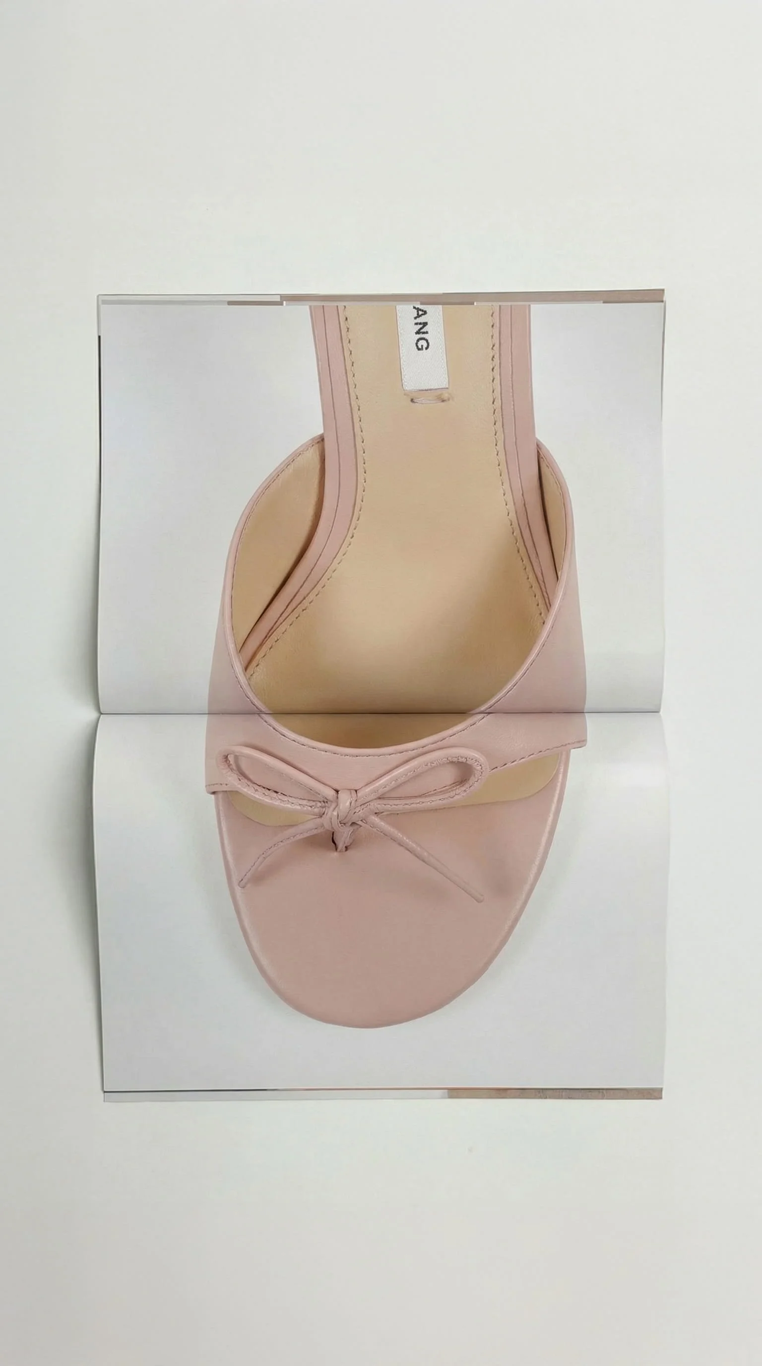 A pink ballet flat shoe with a bow, displayed on a white background with a mirror reflection.