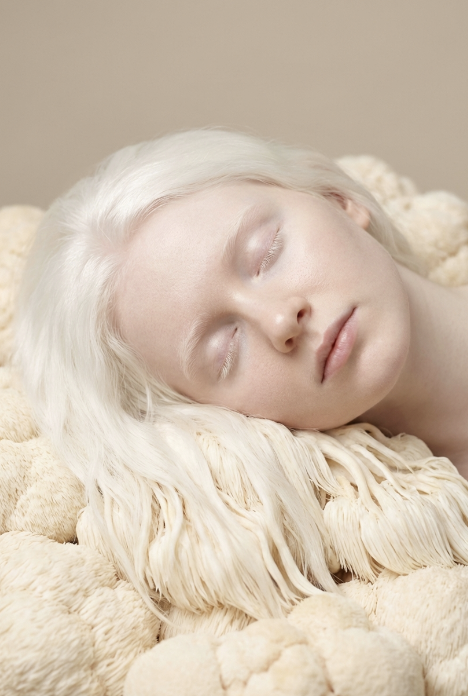 Close-up of a woman with platinum blonde hair peacefully sleeping on a soft, cream-colored textured surface.