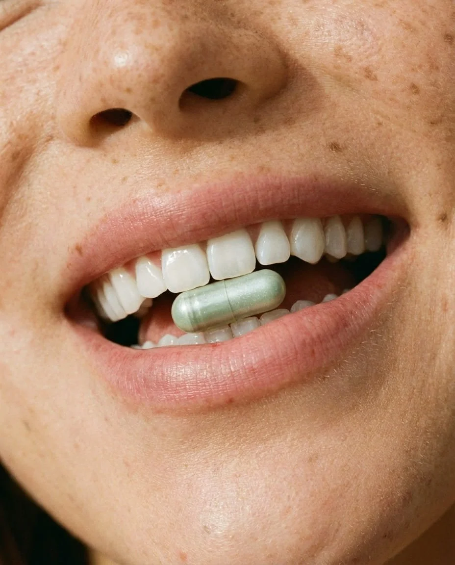 Close-up of a person's mouth with a capsule pill between their teeth.