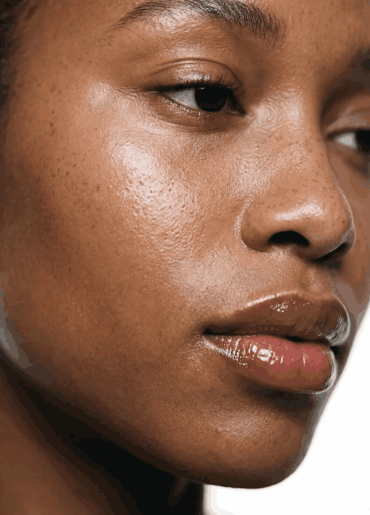 Close-up of a woman's face showing her skin texture, eye, nose, and lips with glossy lipstick.