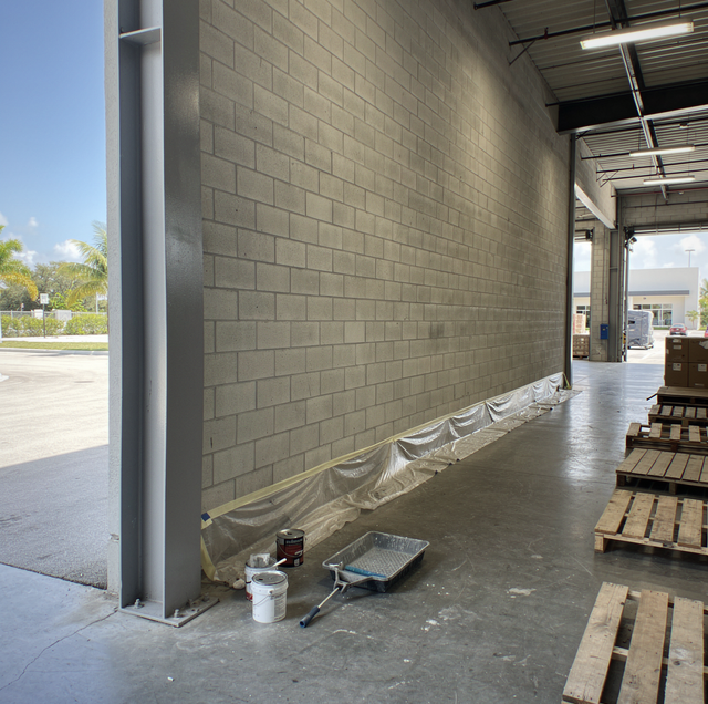 Commercial painters on scaffolding coating a warehouse interior wall