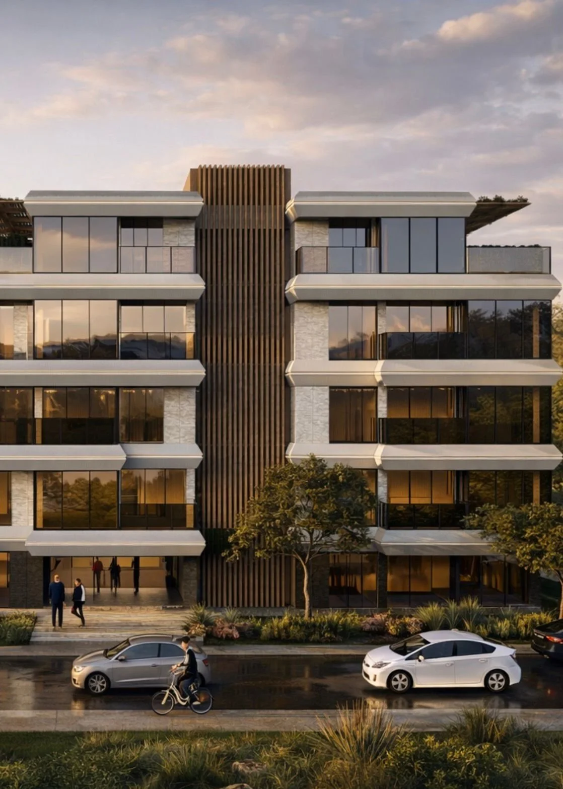 Modern multi-story building with large glass windows and a central wooden feature. People are walking and cars are parked in front with a cyclist passing by. Trees and landscaped greenery are present in the foreground, with a partly cloudy sky at sun