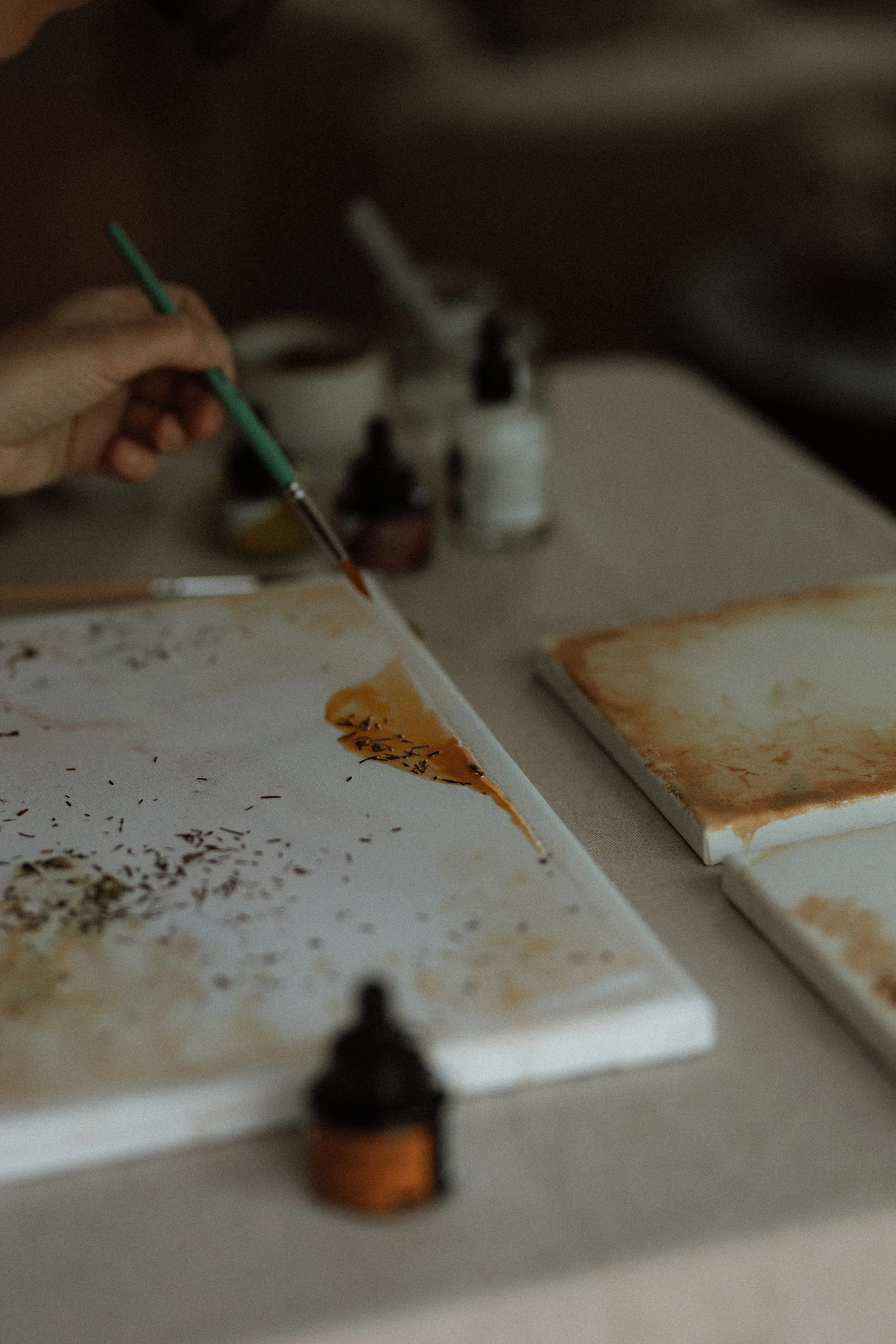 Une main tenant un pinceau au-dessus d'une palette de peinture et des bouteilles de peinture sur la table.
