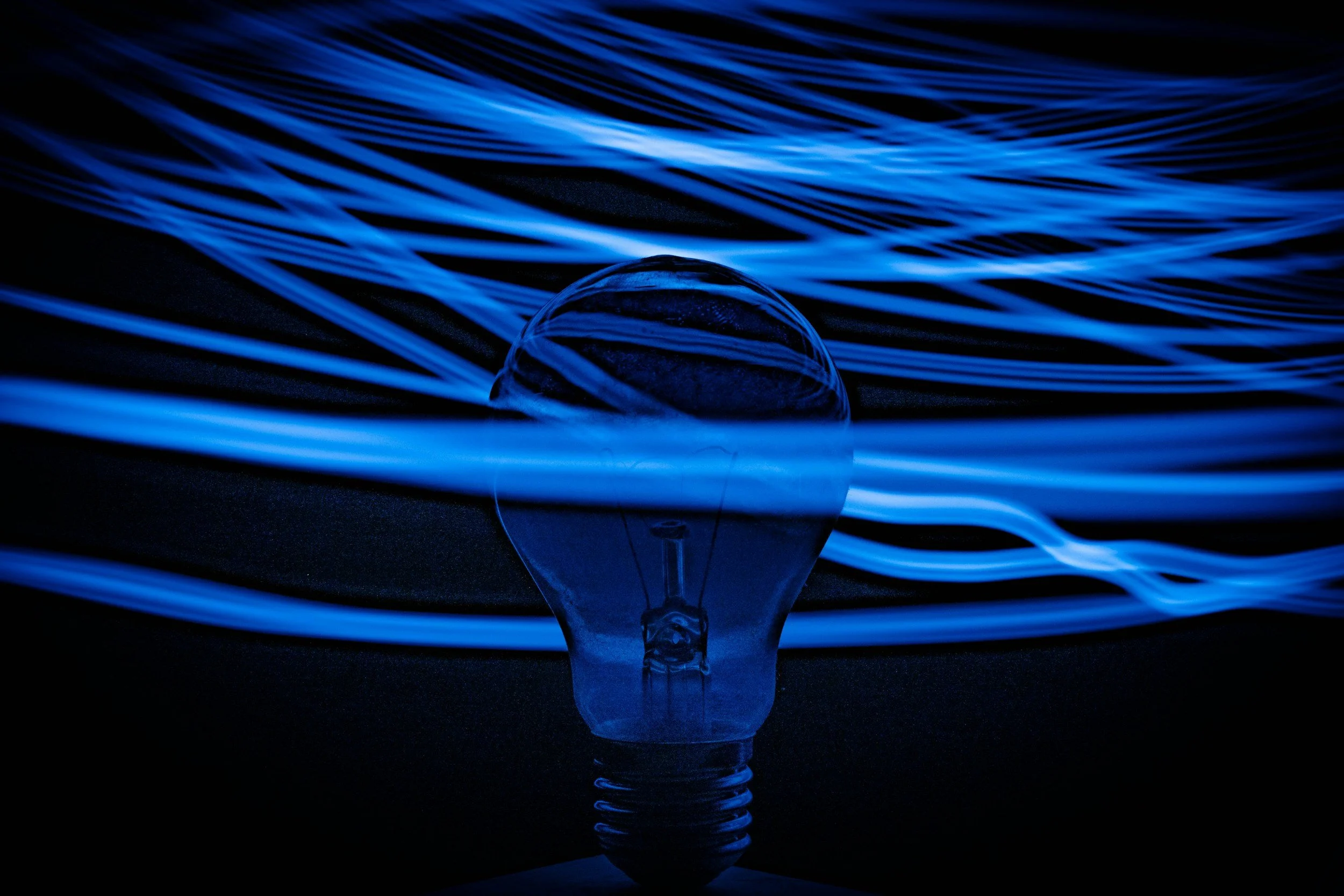 Bombilla de luz encendida con filamentos de luz azul brillante que crean patrones ondulados en la oscuridad.