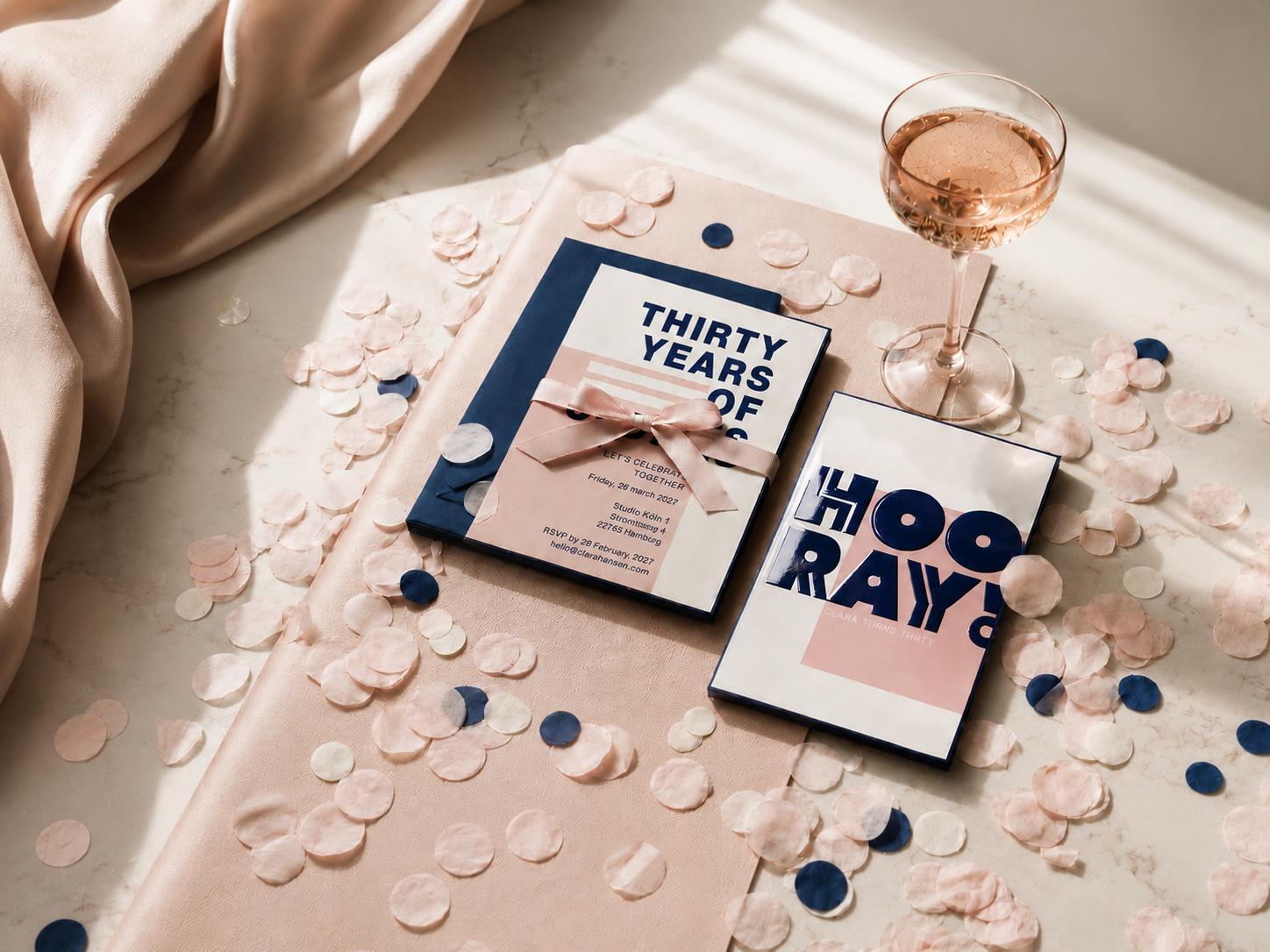 Ein Tisch mit Konfetti in Rosa, Weiß und Blau, sowie zwei Geschenkboxen, ein Glas Roséwein und eine rosa Stoffbahn, für einen Geburtstag im Alter von 30 Jahren.