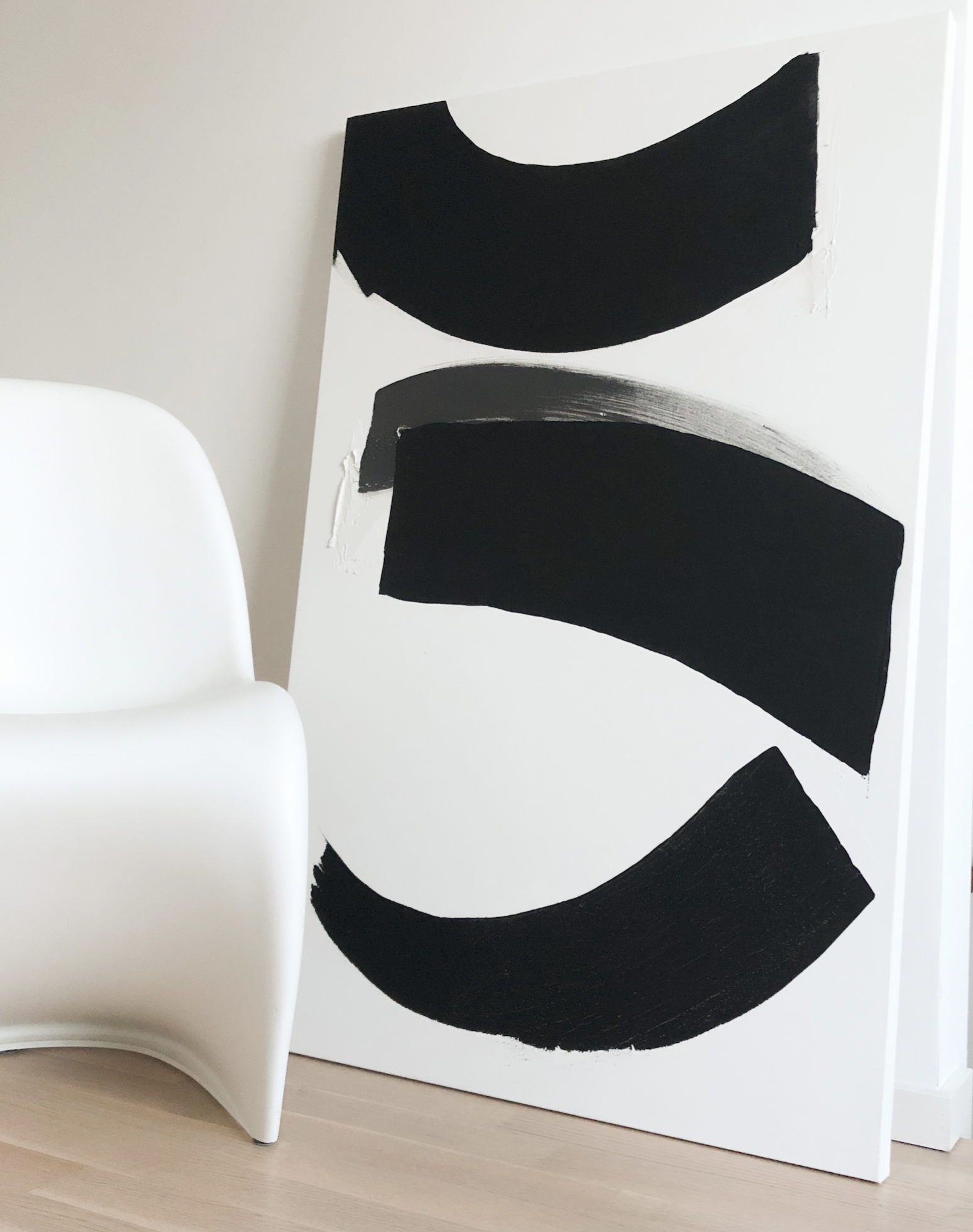 Schwarz-weiße moderne abstrakte Kunst auf einer weißen Staffelei, neben einem weißen Stuhl, auf Holzboden