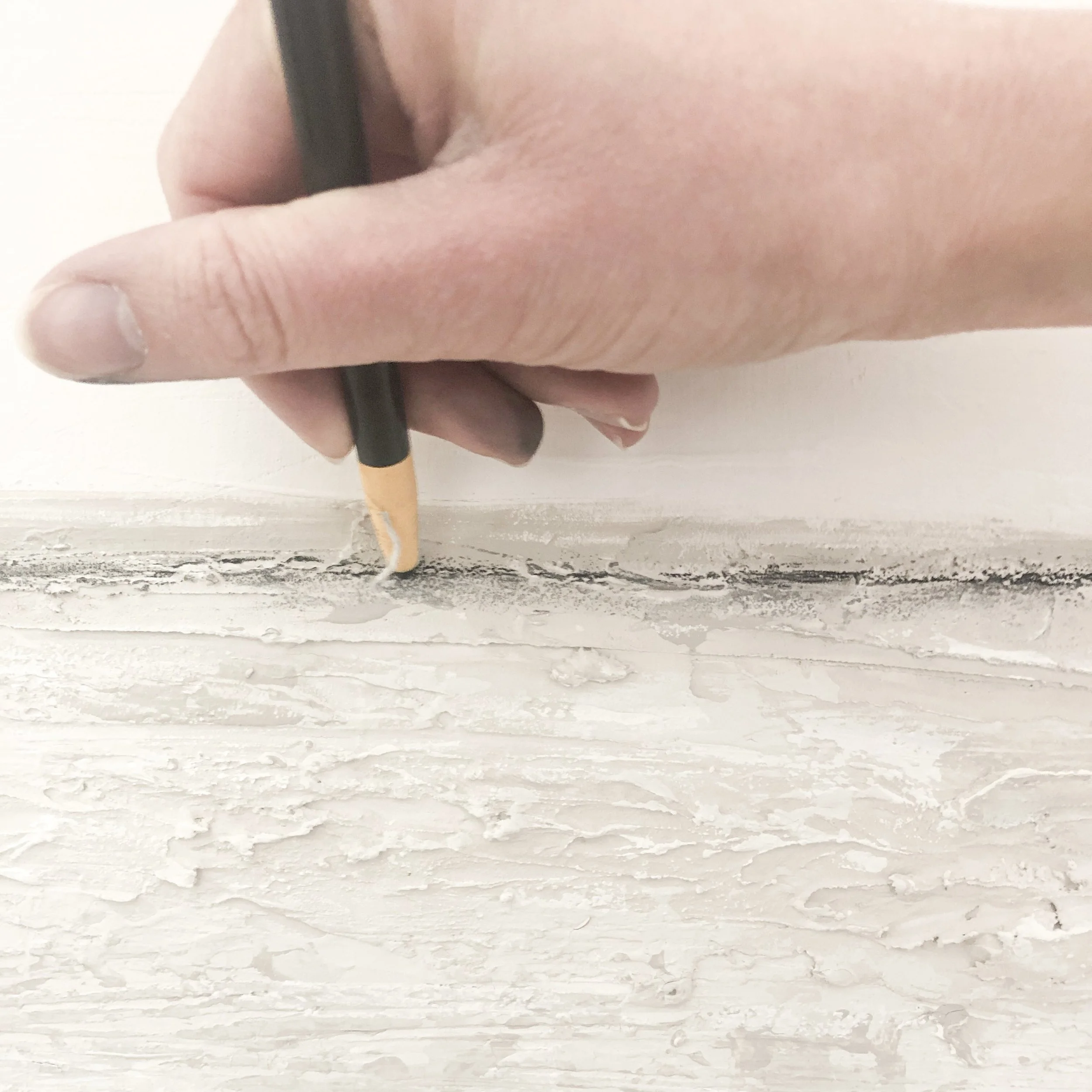 Ein Hand hält einen Bleistift, der sich auf einer weißen Wand befindet.