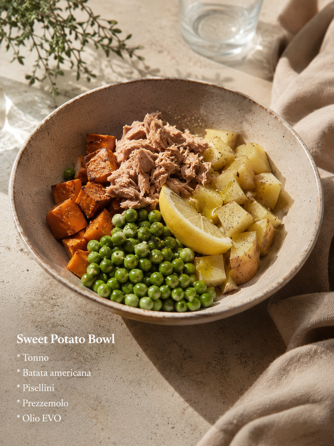 A bowl of sweet potato with chunks of tuna, green peas, and diced potatoes, garnished with lemon wedge and black pepper, on a textured surface with a glass of water in the background and a sprig of greenery nearby.