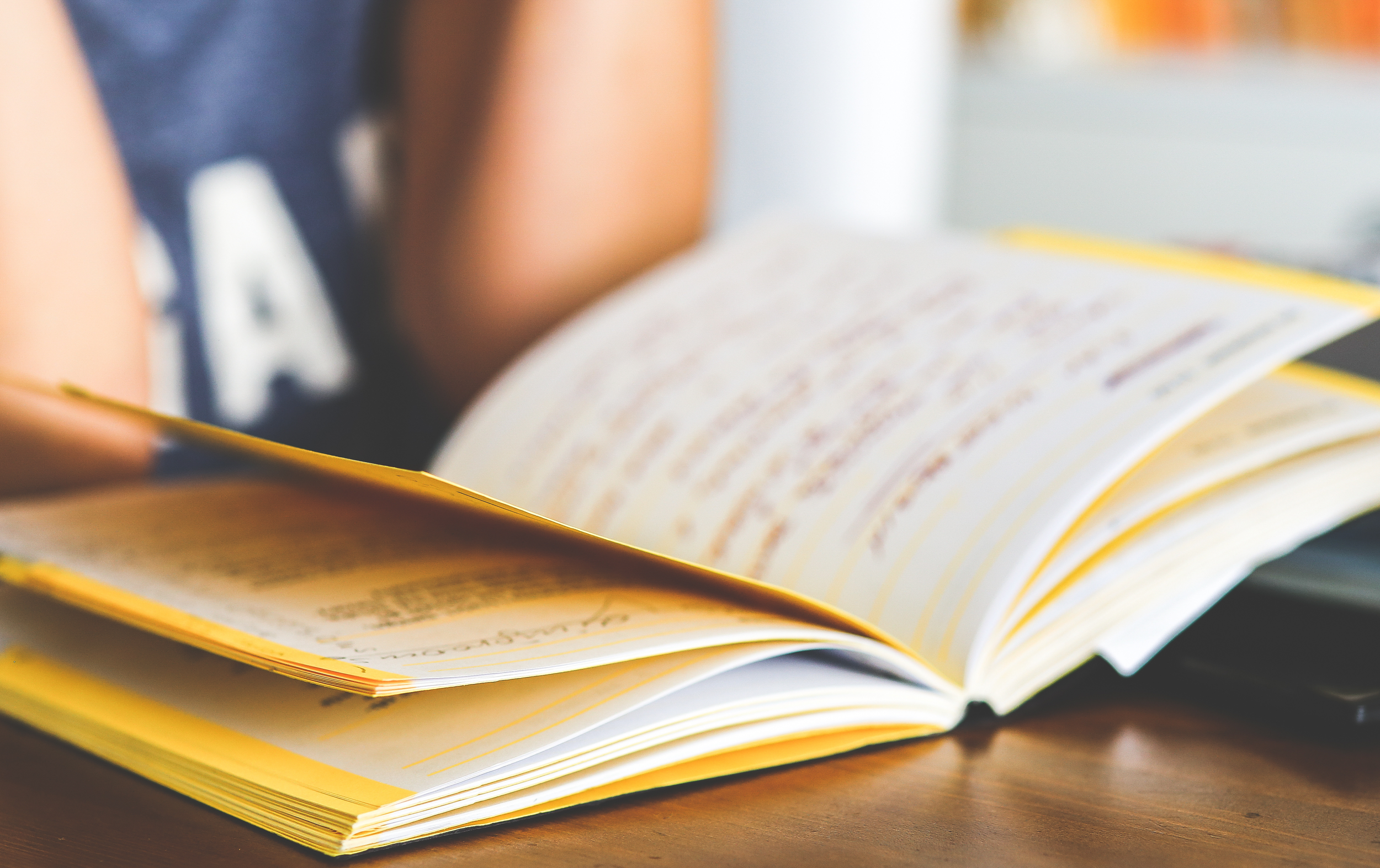 An open book with yellow pages resting on a wooden surface.