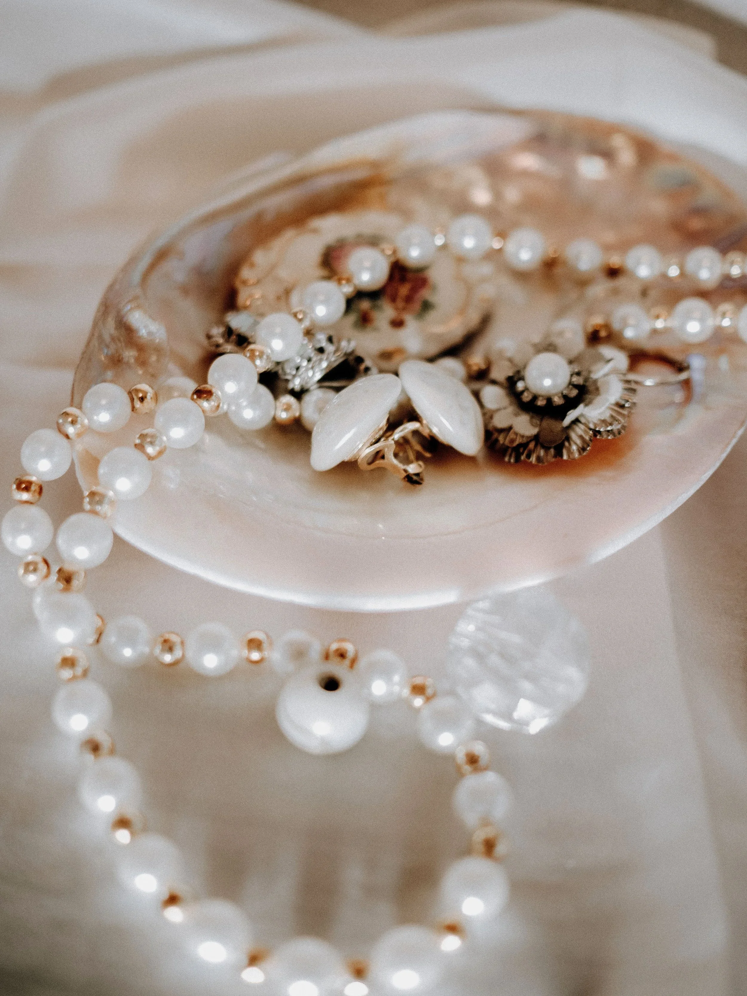 Elegant pearl necklace and vintage earrings displayed on a decorative shell dish with soft natural lighting.