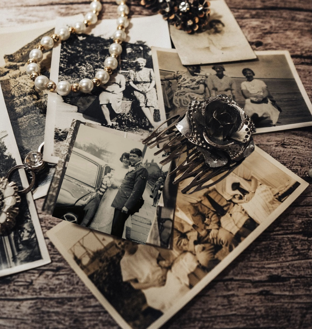 Collection of antique family photographs, pearl jewelry, and a vintage floral brooch arranged on a rustic wooden surface.