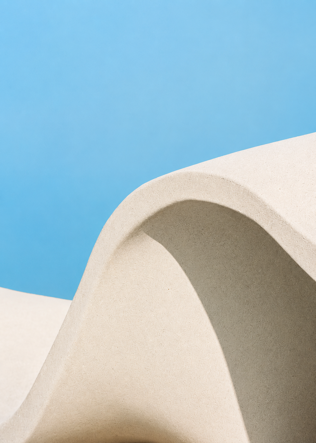 Abstract architectural composition with smooth beige concrete curves against a bright blue sky.