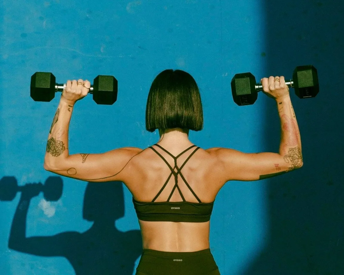 Claris the founder, lifting weights doing a shoulder press with strong athletic back.