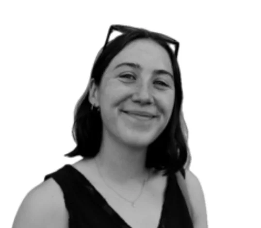 Black and white photo of a woman smiling, wearing glasses on her head, a sleeveless top, and a necklace.