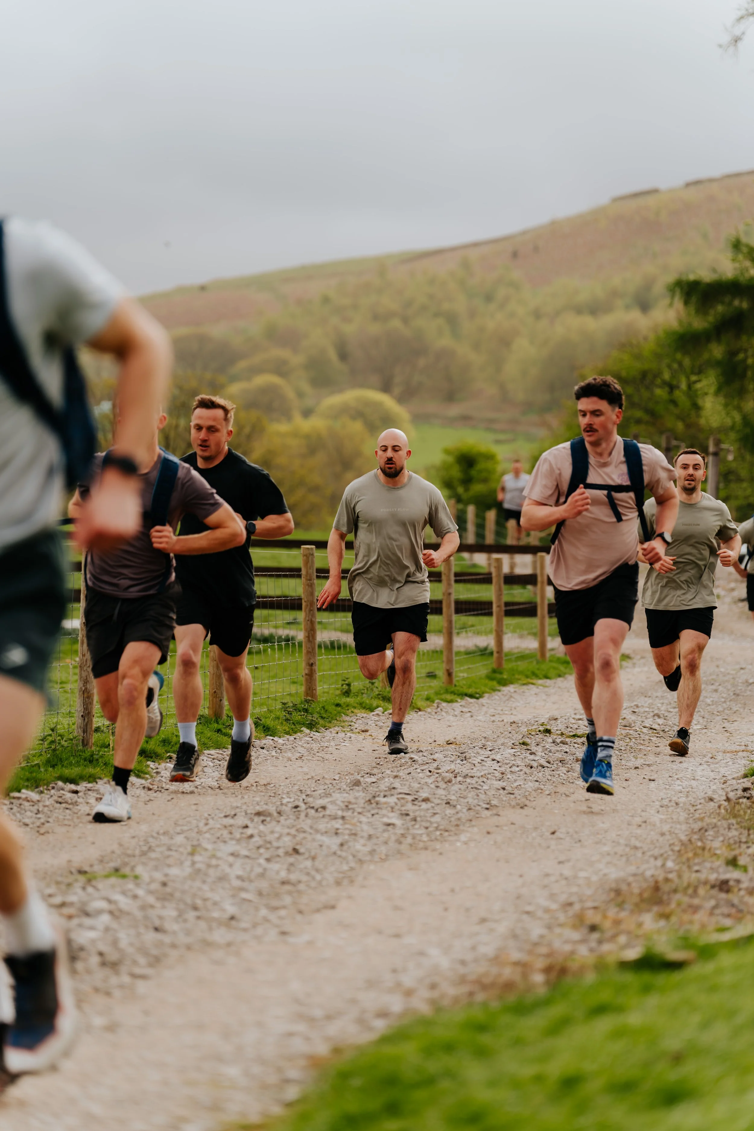 Group of men running outdoors on a gravel trail with green hills and trees in the background.