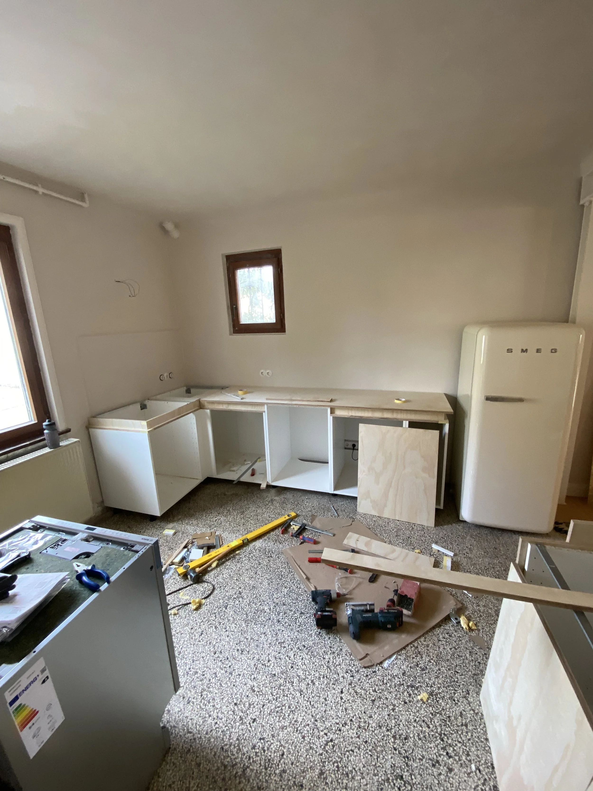 Ein Raum, der gerade renoviert wird, mit Werkzeugen, Baumaterialien und unvollendeten Küchenschränken auf dem Boden.