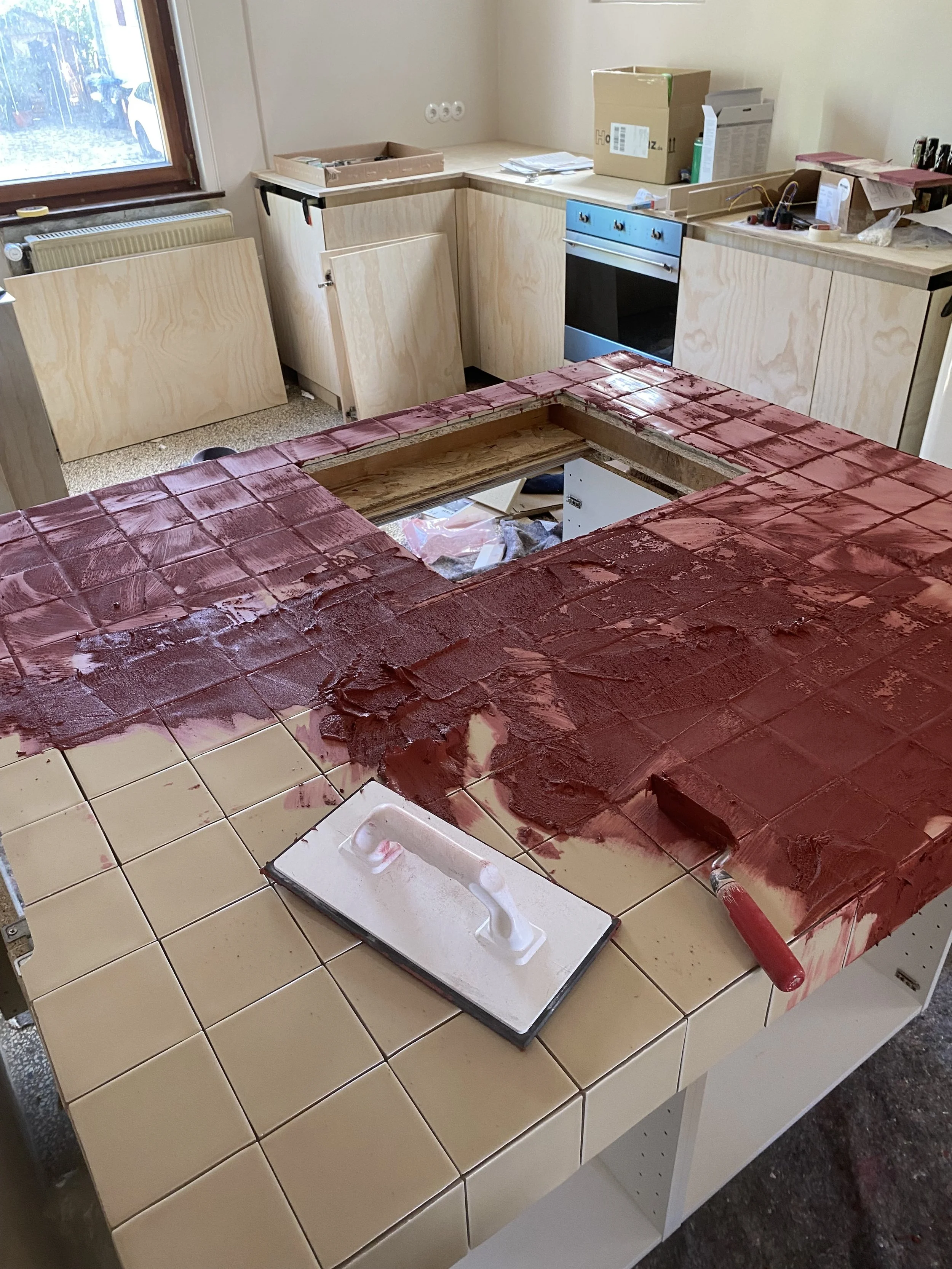 Küche im Umbau mit ausgebautem Küchenblock, teilweise verkleideten Arbeitsplatten, Geschirr, Pinsel und Baumaterialien