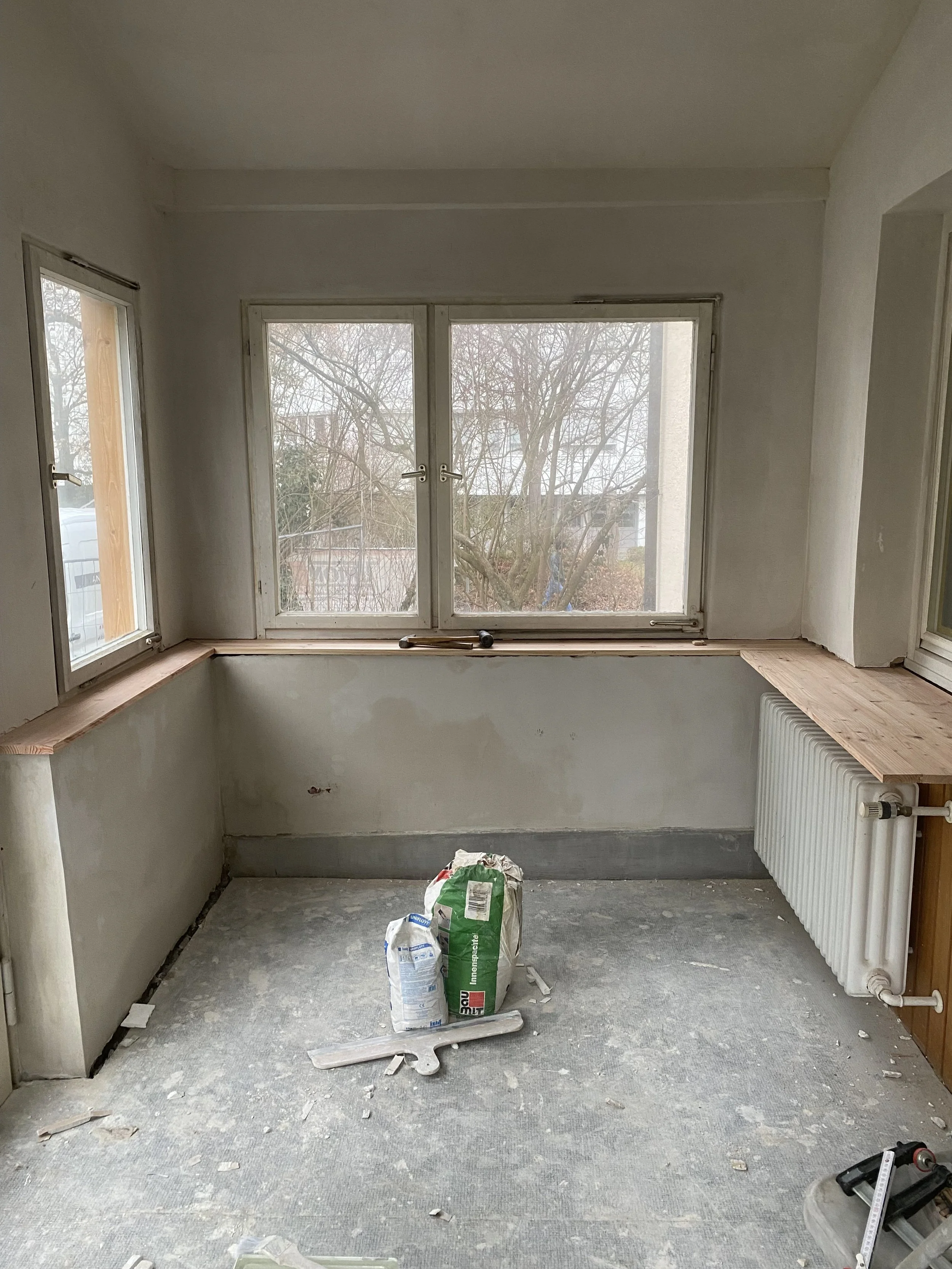 Ein unfertiges Zimmer mit Fenster, auf dem Boden liegt Baumaterial, vermutlich für den Ausbau oder die Renovierung.