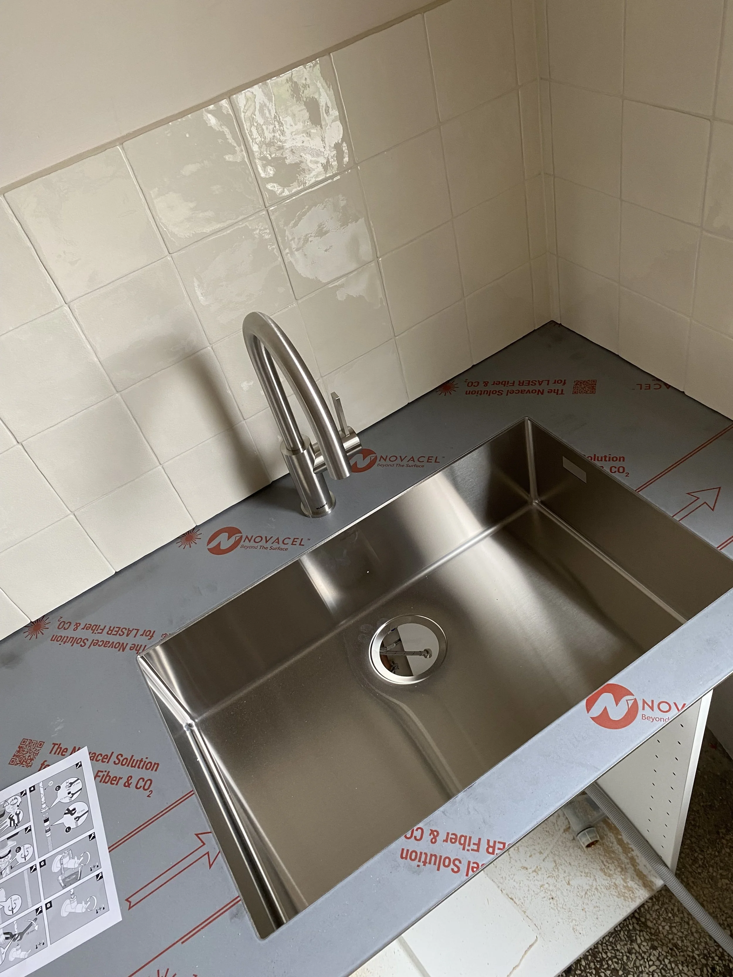 Ein Edelstahl-Spüle mit Wasserhahn in einem Geschäftsraum, umgeben von Informationsmaterial und Firmenlogos.