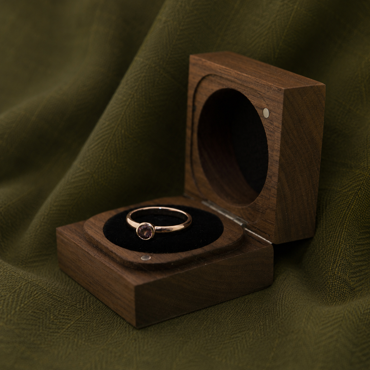 A gold ring with a purple gemstone in a wooden ring box on green fabric.
