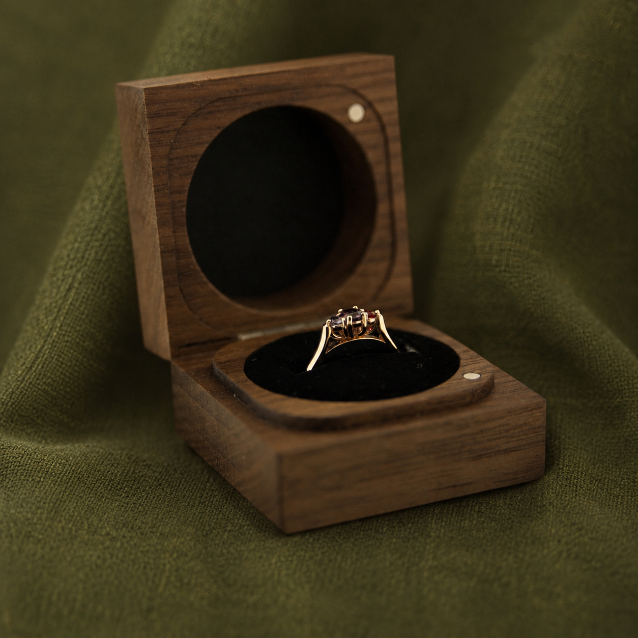 A gold ring with a dark gemstone in a wooden ring box on green fabric.