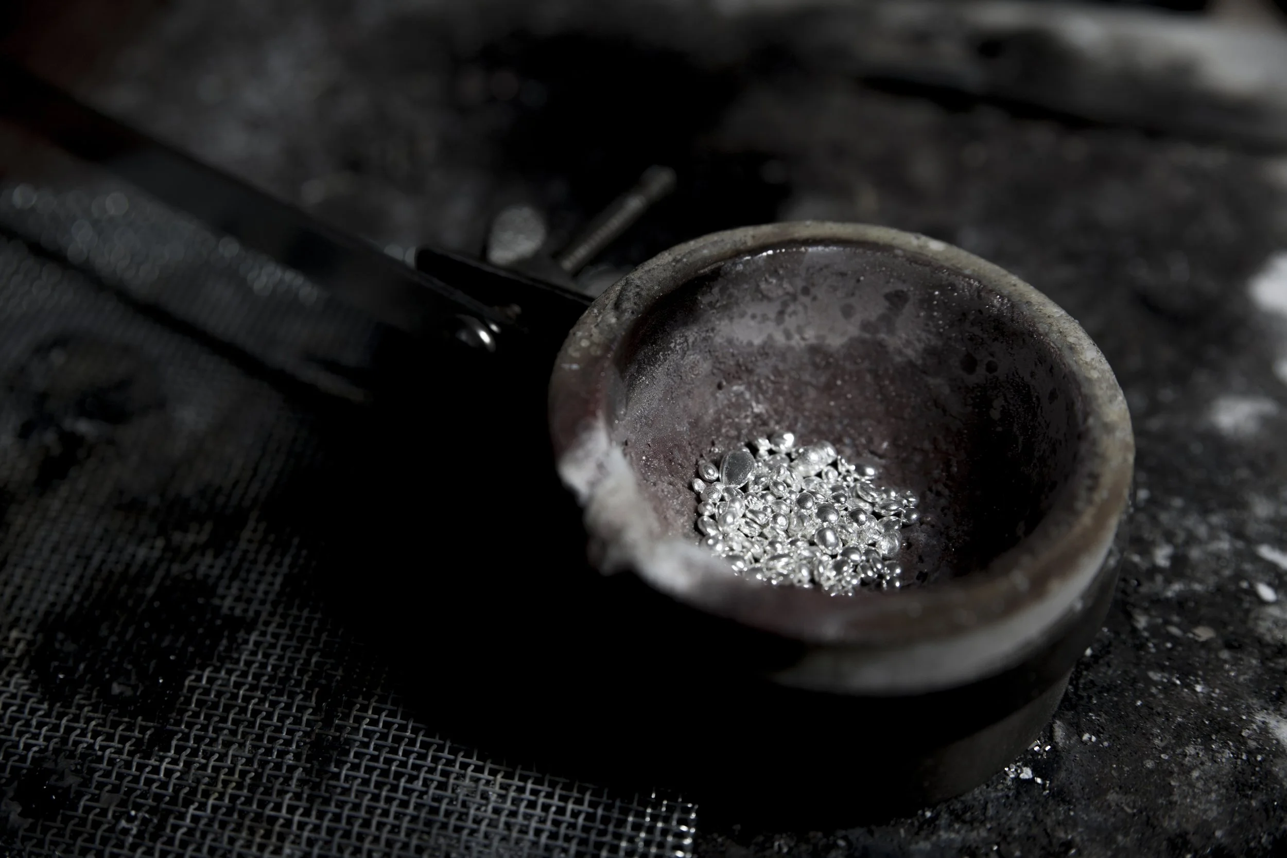 A small container with silver beads inside, surrounded by a dark, textured surface.