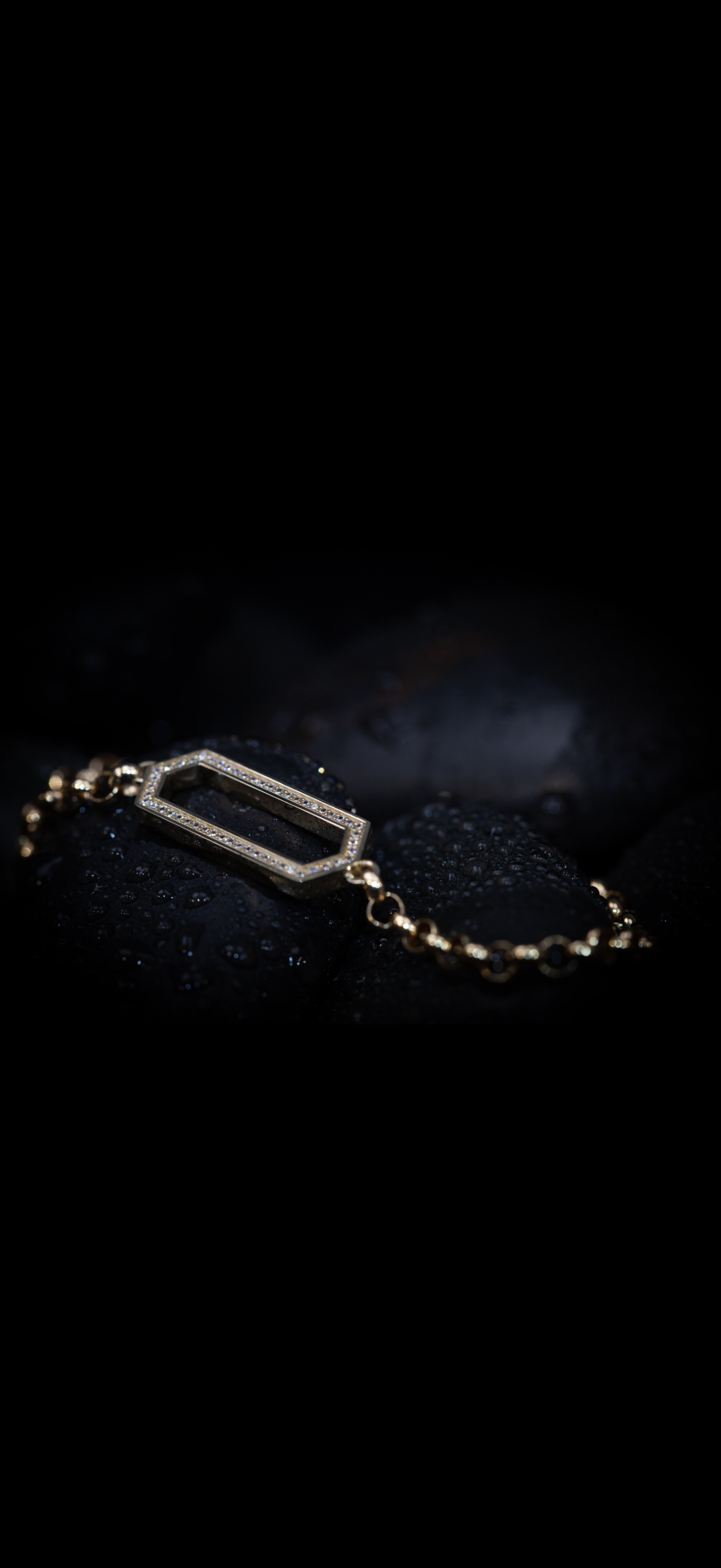 Gold bracelet with a rectangular open frame and small diamonds, resting on dark wet rocks