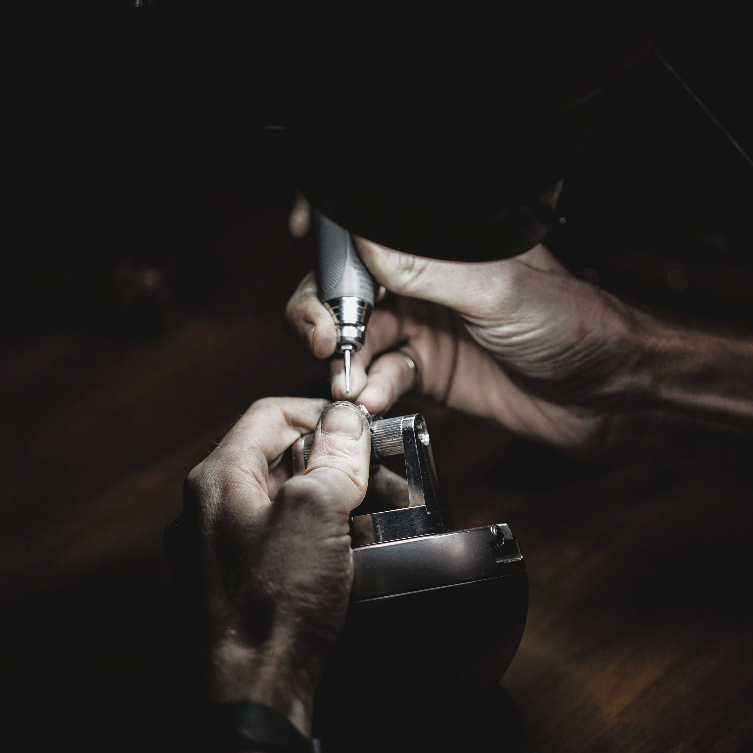 Close-up of a jeweller's hands holding a micromotor, performing diamond setting in a dark environment.
