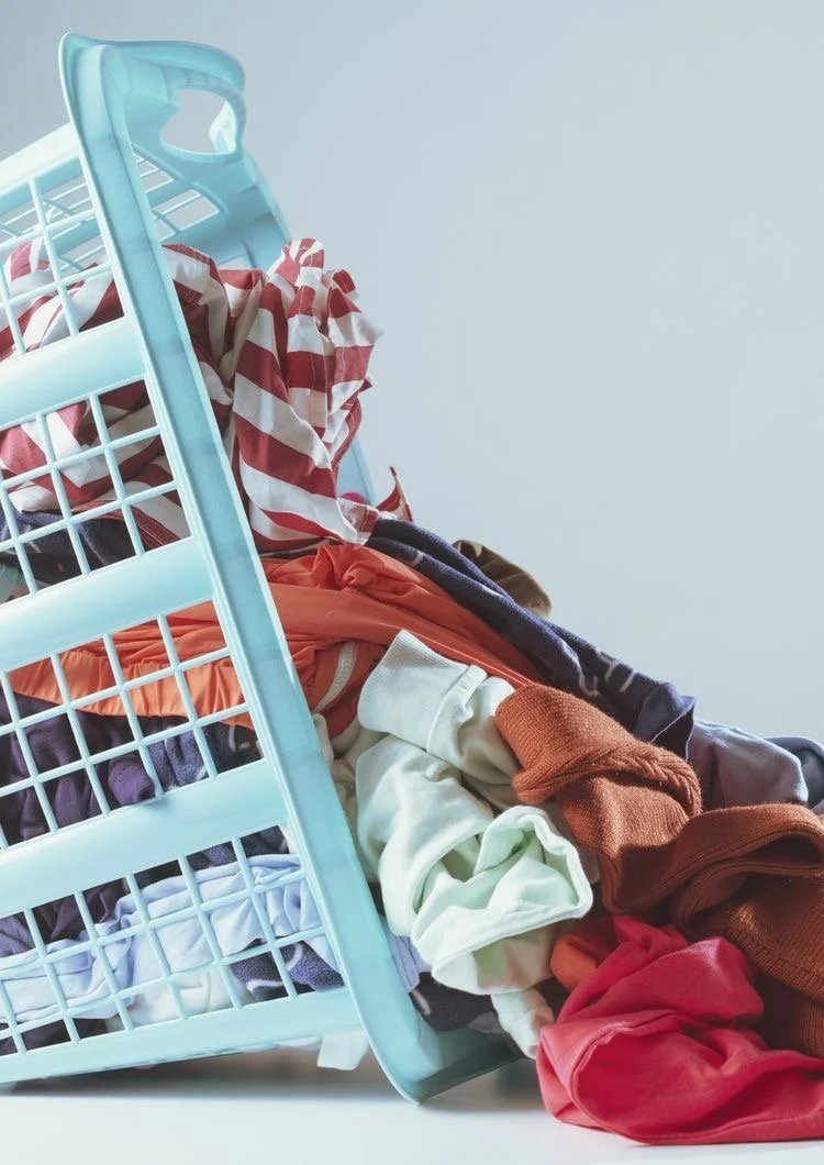 A tilted laundry basket spilling multicolored clothes onto a white surface.