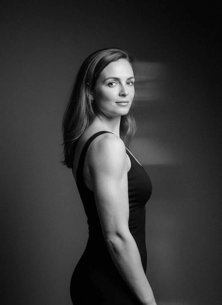 Black and white portrait of a woman with shoulder-length hair, wearing a sleeveless black top, looking over her shoulder.