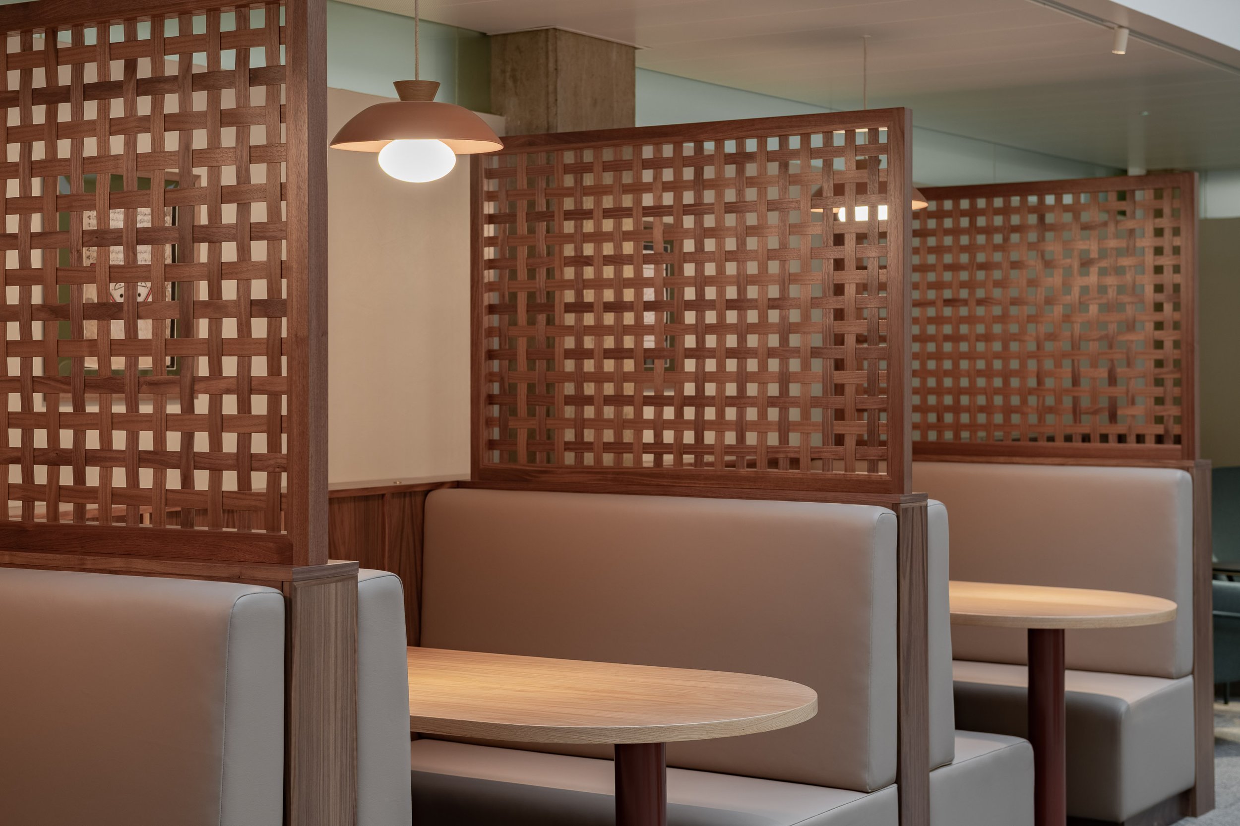 Modern restaurant interior with cream upholstered booths, rounded wooden tables, pendant lighting, and decorative bespoke wooden lattice divider screens in walnut. Workplace interior design Bristol South West, and workplace fit out.