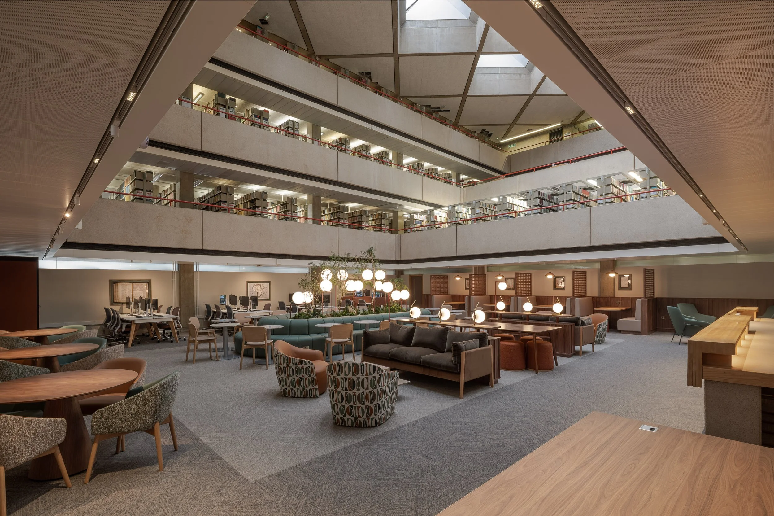 SOAS University of London Library Interior Design. Modern multi-level library interior with bookshelves, study tables, lounge seating, and globe lamps.