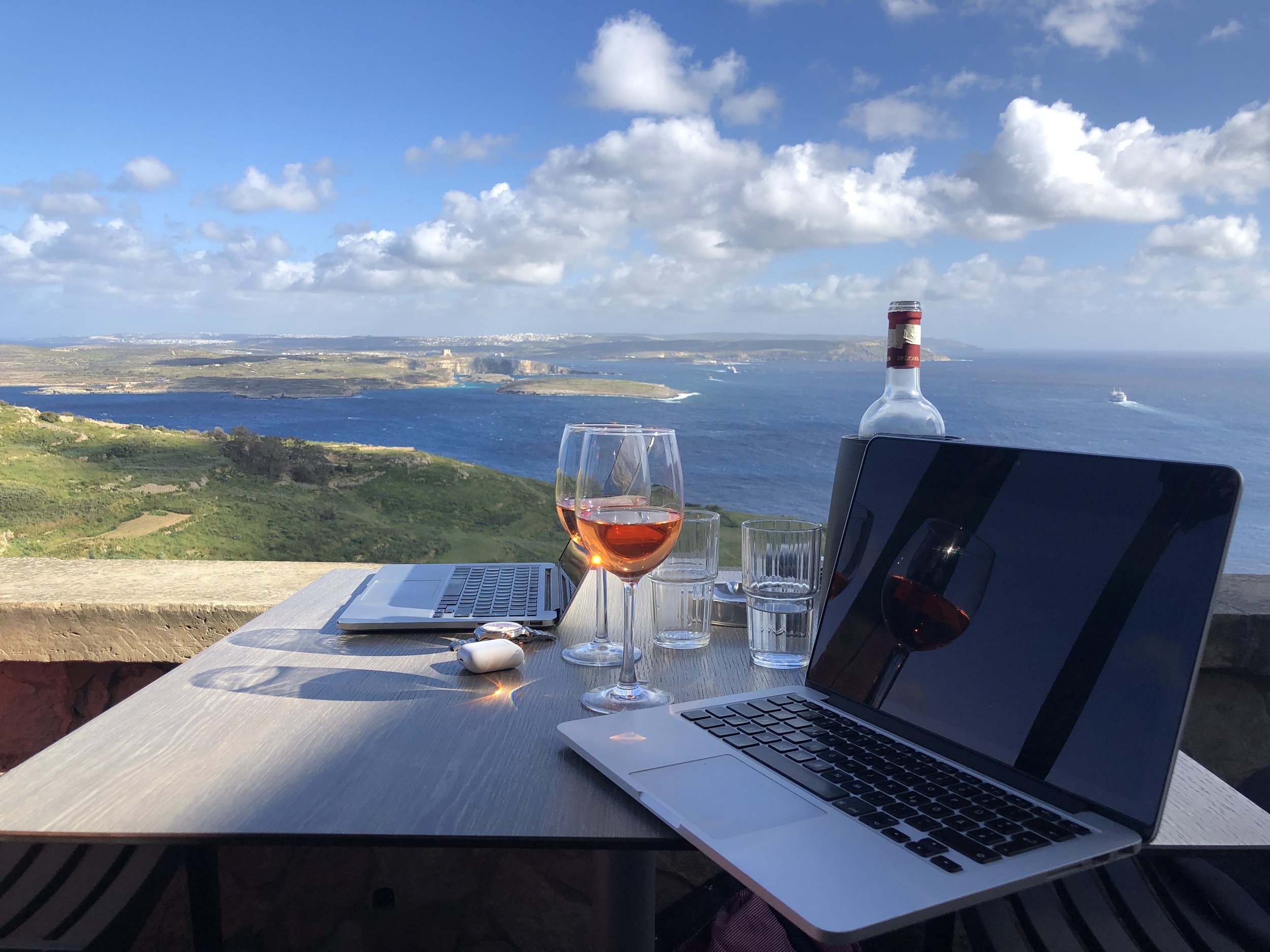 Laptop und Weingläser mit Blick auf Malta