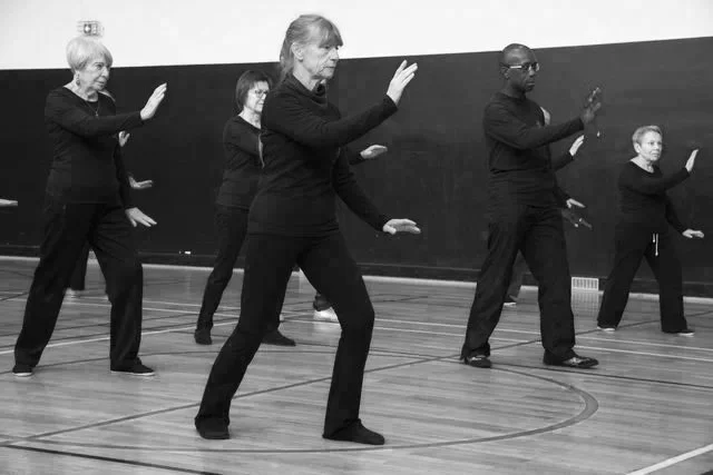 Groupe de six personnes âgées pratiquant la tai-chi dans une salle de sport